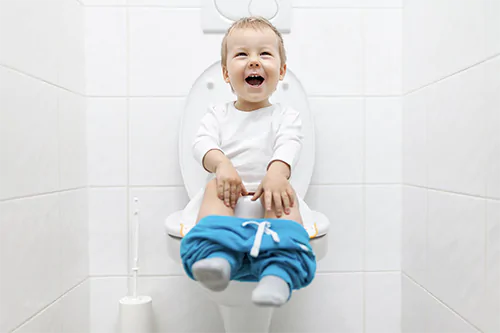 Jak nauczyć dziecku korzystać z sedesu? Mały uśmiechnięty chłopiec siedzi na toalecie.