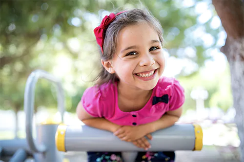 Jak rozwijać kreatywność u dzieci? Mała dziewczynka na placu zabaw uśmiecha się do aparatu.