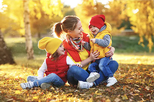 Jak wzmocnić odporność u dzieci? Kolorowa ubrana mama z dziećmi bawi się w jesiennych liściach.