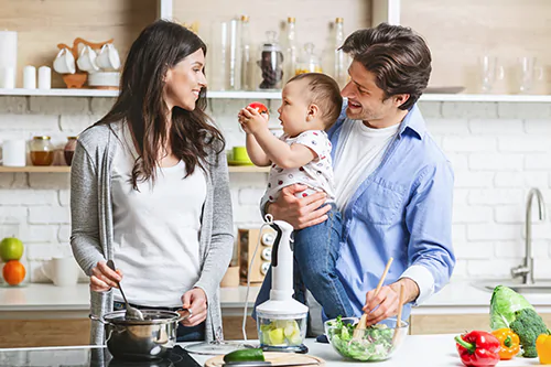Probiotyk na jelita - w jaki sposób odbudowuje florę bakteryjną? Szczęśliwa rodzina - mama, tata i małe dziecko - przygotowują wspólnie posiłek w kuchni.