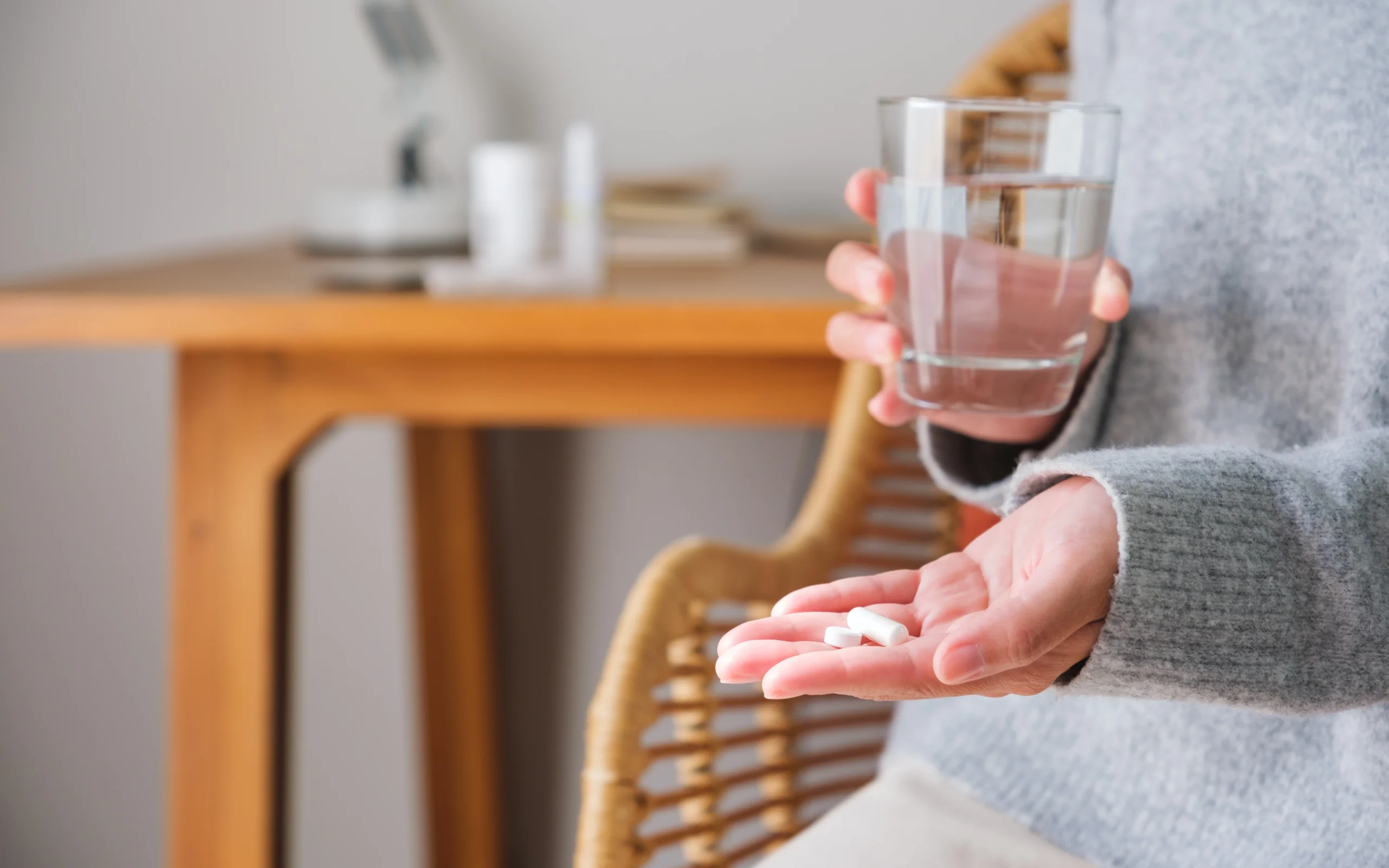 Probiotyk – przed czy po antybiotyku? Kiedy brać probiotyki – rano czy wieczorem? Kobieta trzyma w dłoniach 2 kapsułki probiotyku i szklankę wody.