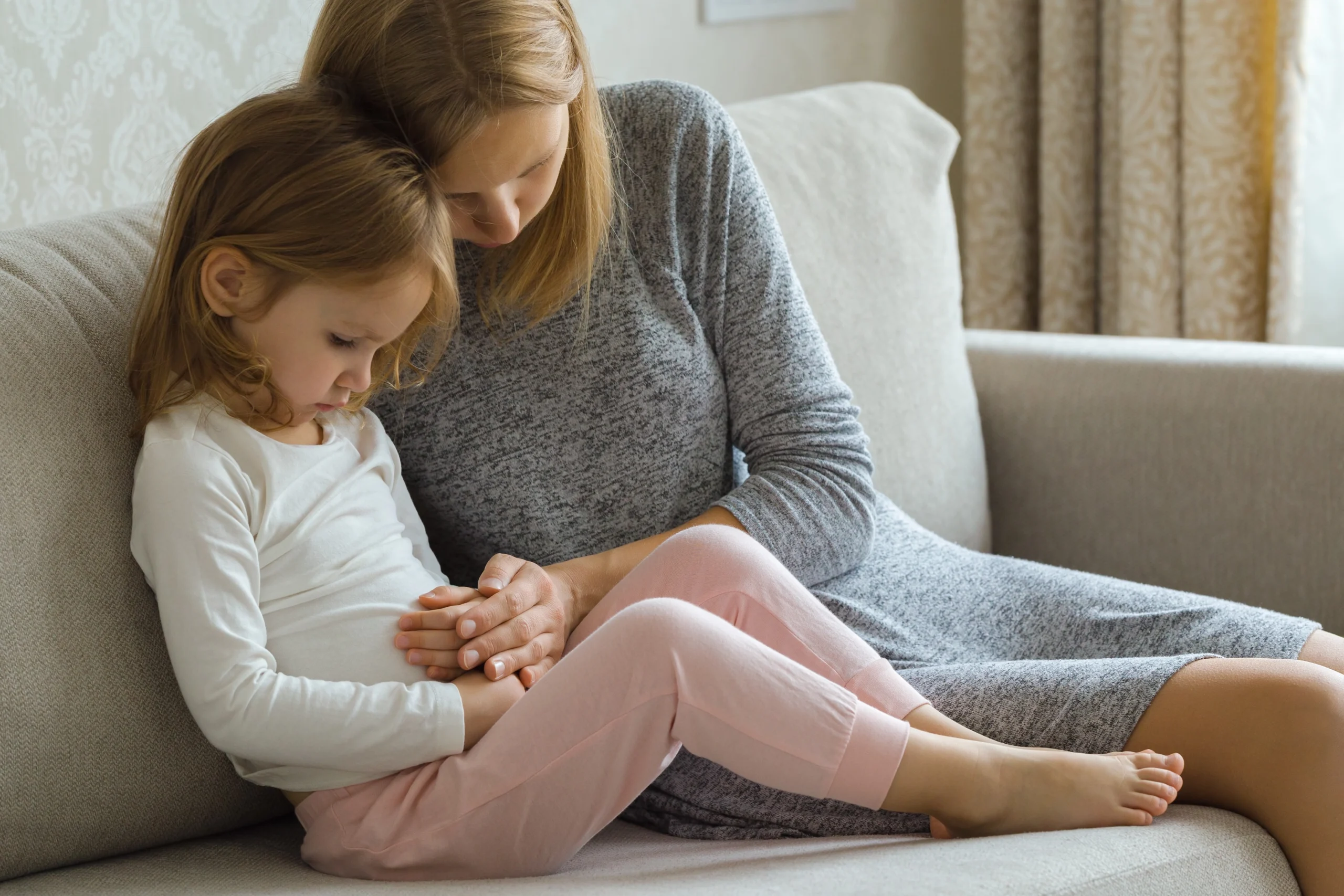 Jak poprawić mikrobiom jelitowy u dziecka? Mama masuje córeczkę po bolącym brzuszku.