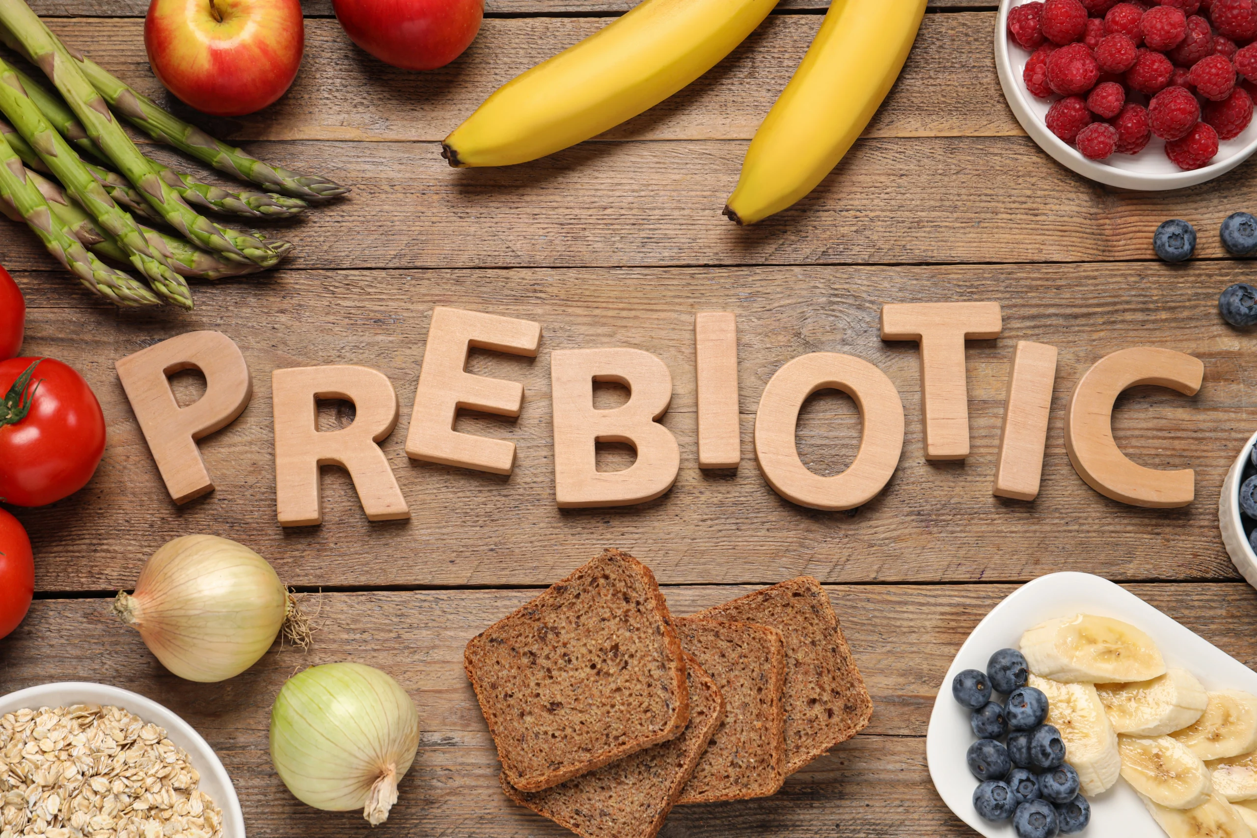 Prebiotyki - czym są i jak działają? Na drewnianym stole leżą produkty żywieniowe bogate w probiotyki, a na środku leżą drewniane literki ułożone w słowo prebiotic.