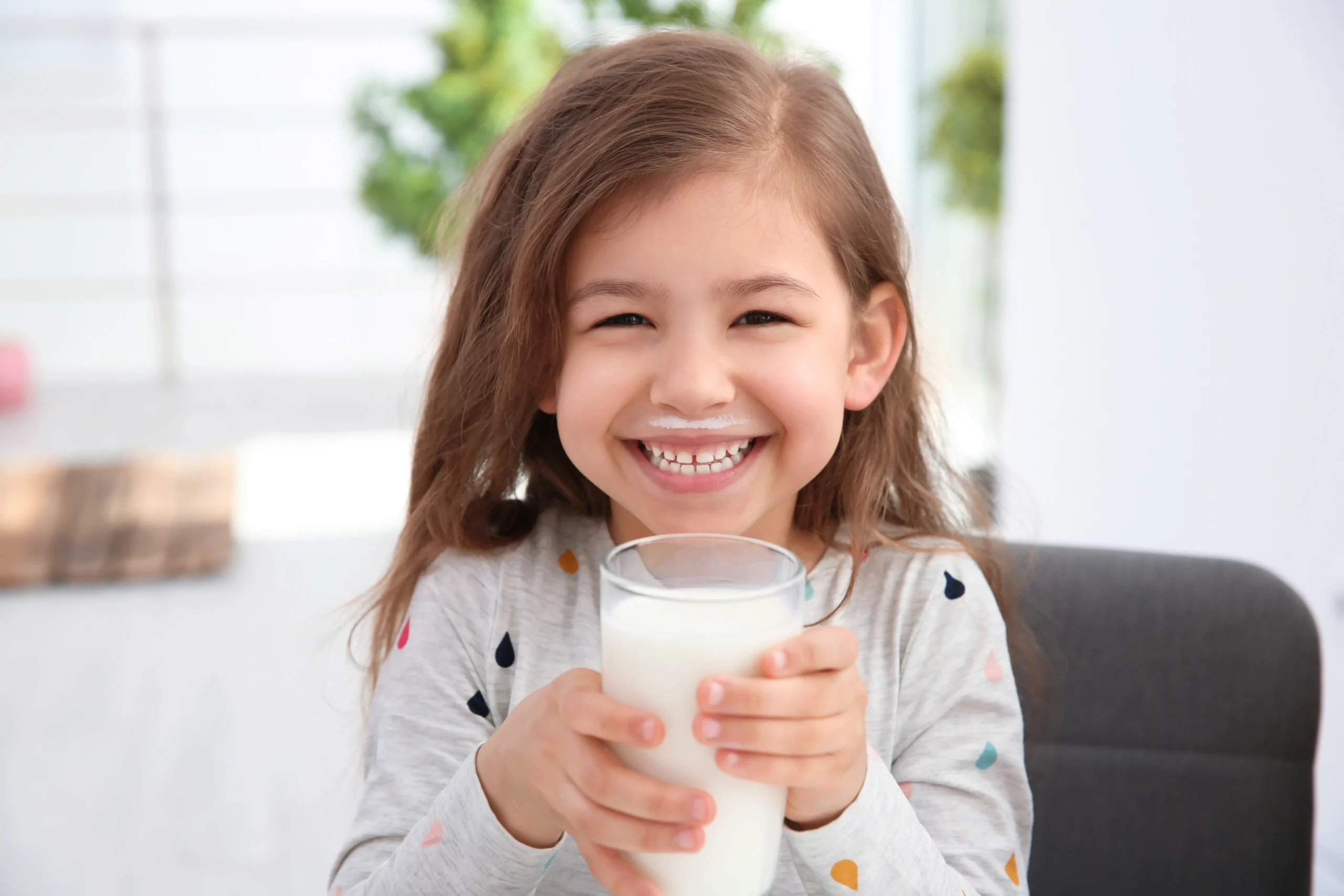Synbiotyki dla dzieci - kiedy warto je stosować? Mała dziewczynka pije mleko ze szklanki i uśmiecha się do aparatu.