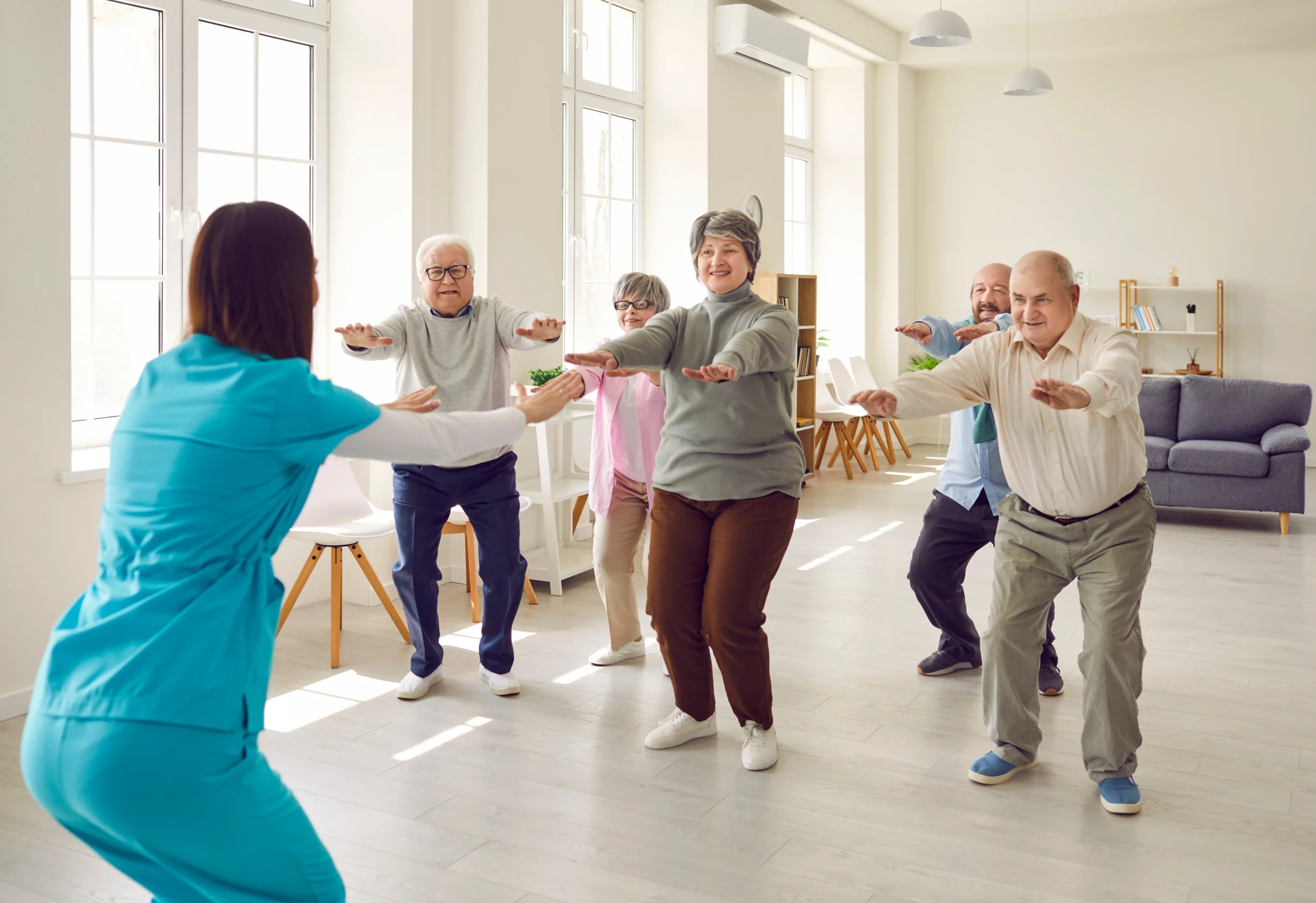 Jak dbać o zdrowie po 60. roku życia? Seniorzy ćwiczą w sali z fizjoterapeutką.